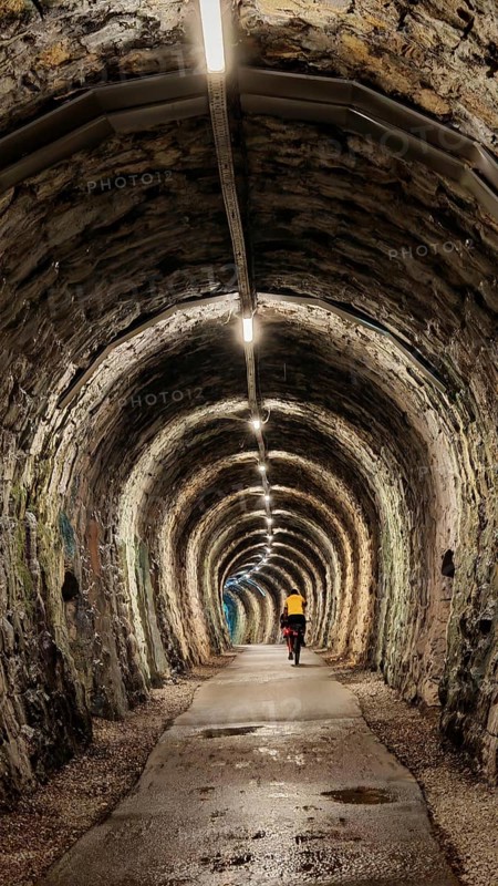 An illuminated tunnel with stone walls and a cyclist in the distance, Slovenia