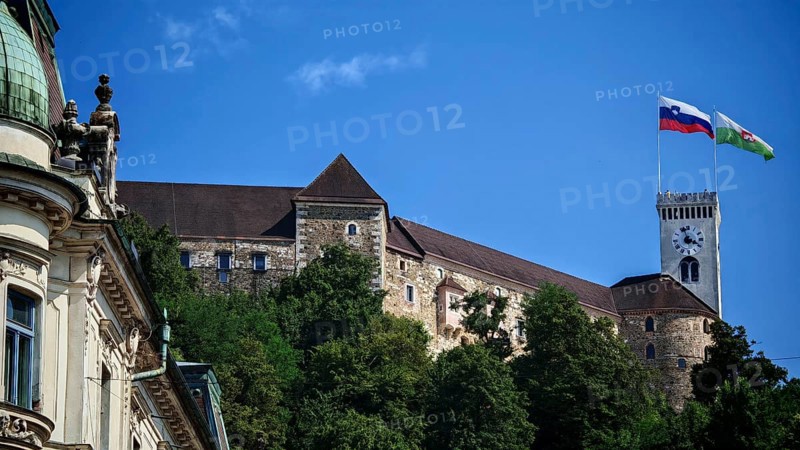 Mighty castle with two flags on a tower nestled in green trees against a clear sky, Ljubljana, Slovenia