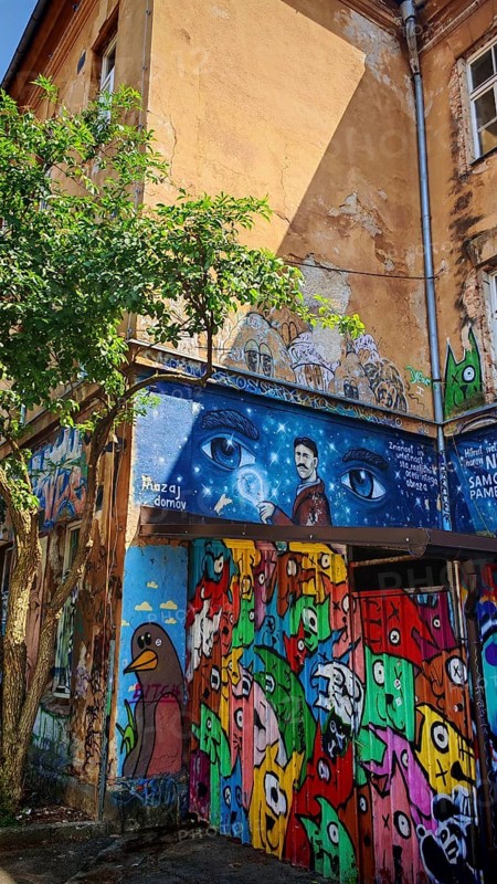 Colourful graffiti and art on a building wall with trees and various figures, Ljubljana, Slovenia