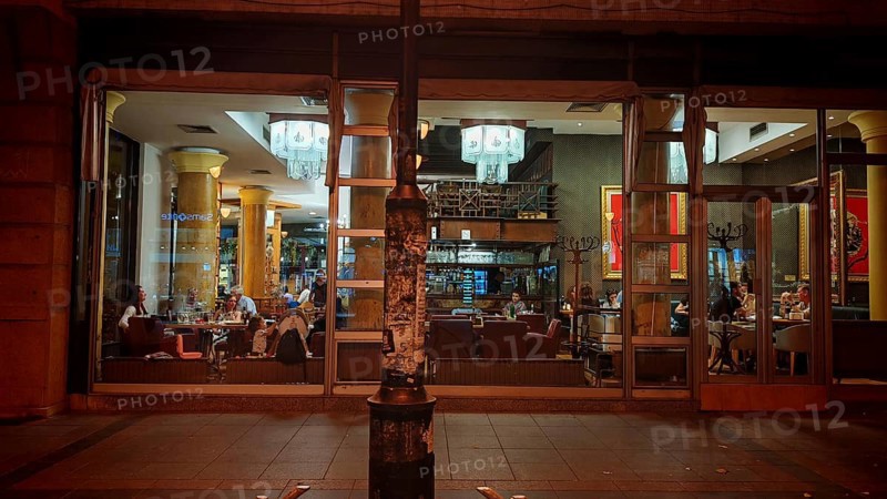 Interior view of a café with glass façade and visible guests at night, Skopje, North Macedonia