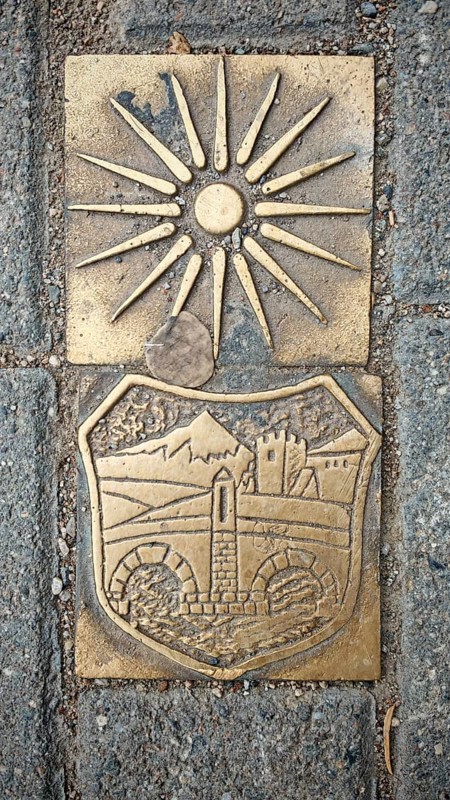 Metal relief with sun symbol and historical depiction on a stone surface, Skopje, North Macedonia