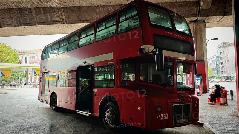 Classic red double-decker bus at a bus stop in an urban environment under a bridge, Skopje, North Macedonia