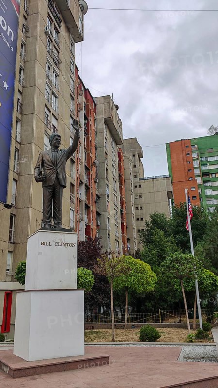 Bill Clinton statue in front of an apartment block with surrounding trees and flagpoles, Pristina, Kosovo
