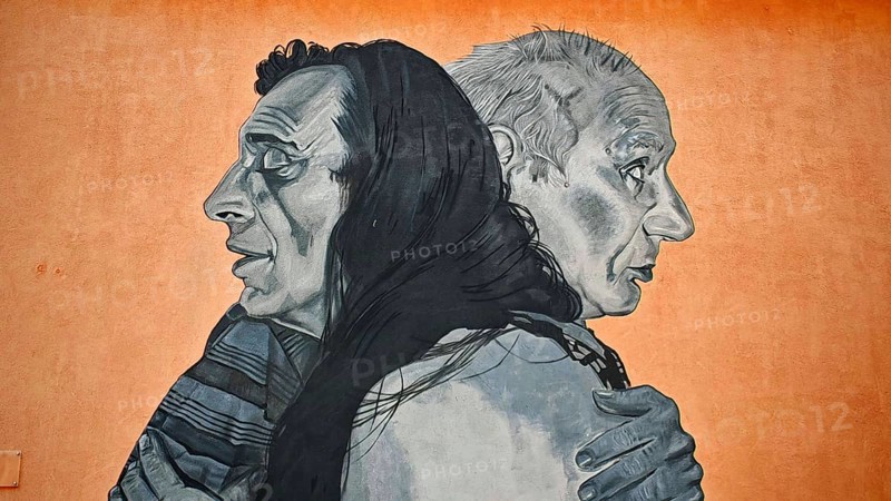 Large mural with two people hugging against an orange background, Pristina, Kosovo