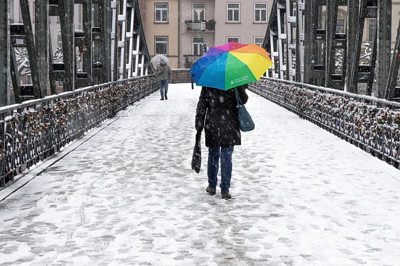 A passer-by walks across the Iron Bridge in Frankfurt am Main with an umbrella. Heavy snowfalls have caused another onset of winter in the Main metropolis, Osthafen, Frankfurt am Main, Hesse, Germany