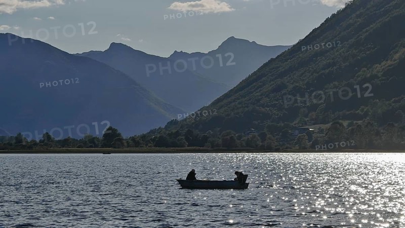 A boat with two people on a lake surrounded by mountain silhouettes in the evening light, Lake Plav, Montenegro