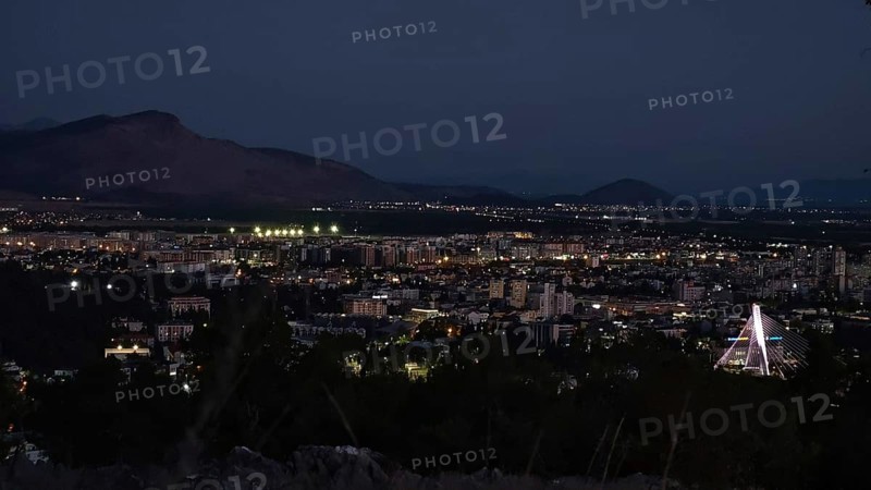 Nighttime city view with illuminated buildings, mountains in the background and dark sky, Podgorica, Montenegro