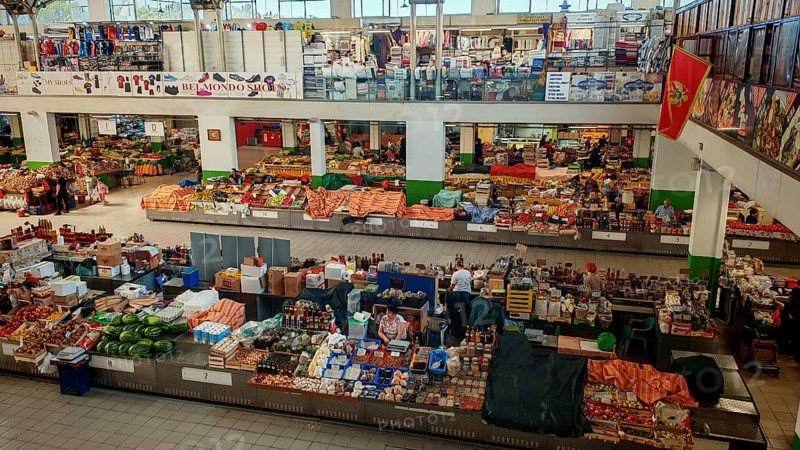 Large market hall with numerous stands and products. People buy fresh food. Lively atmosphere, Ulcinj, Montenegro