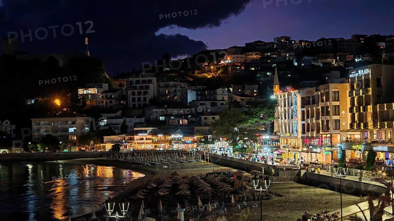 A nighttime beach view with illuminated buildings and dark skies in a lively coastal town, Ulcinj Promenade, Montenegro