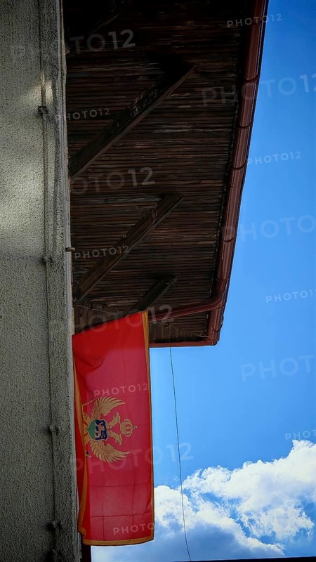 A Montenegrin flag flies on a wooden roof under a clear blue sky, Montenegro