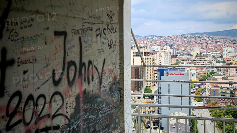 A graffiti-covered building offers a view of an urban landscape under a cloudy sky, Pristina, Kosovo