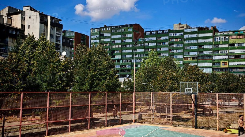 A basketball court surrounded by apartment blocks and trees, in sunny weather, Pristina, Kosovo