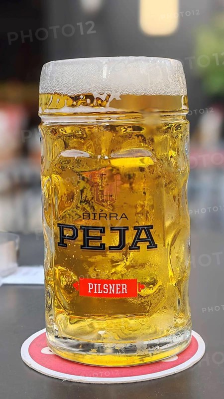Clear beer glass with foam crown on a table in a lively environment, Peja, Kosovo
