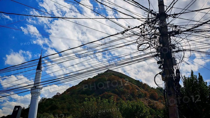 Several power lines in front of a minaret and a wooded hill, Prizren, Kosovo
