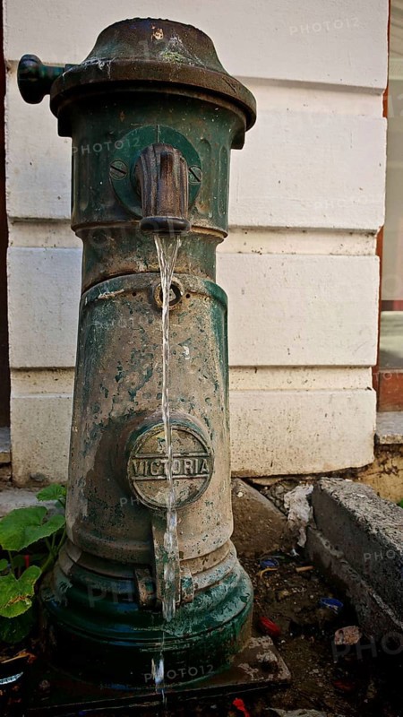 Old green hydrant with Victoria inscription with water flow in front of a wall, Kosovo