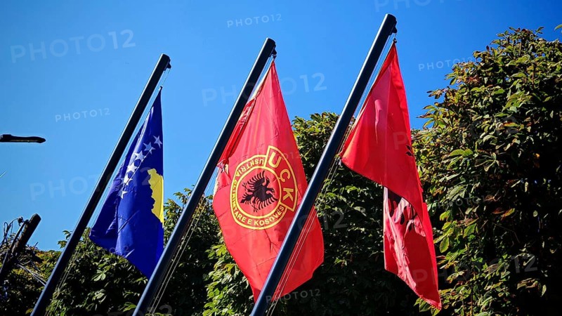 Three flags of Kosovo, USK, Albania fly against green background and blue sky, Kosovo