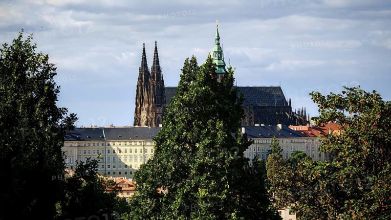 Gothic church between tall trees, cloudy sky in the background, view of Hradcany, Prague, Czech Republic