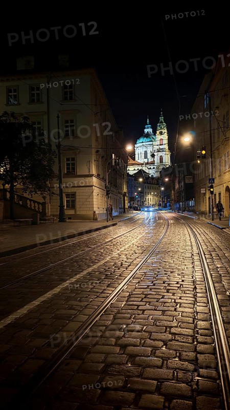 Illuminated cobblestone street with tram tracks at night with a view of a cathedral, Prague, Czech Republic