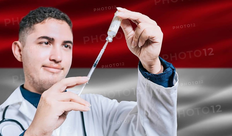 Doctor holding syringe on Monaco flag background. Medical professional holding syringe with Monegasque flag in the background