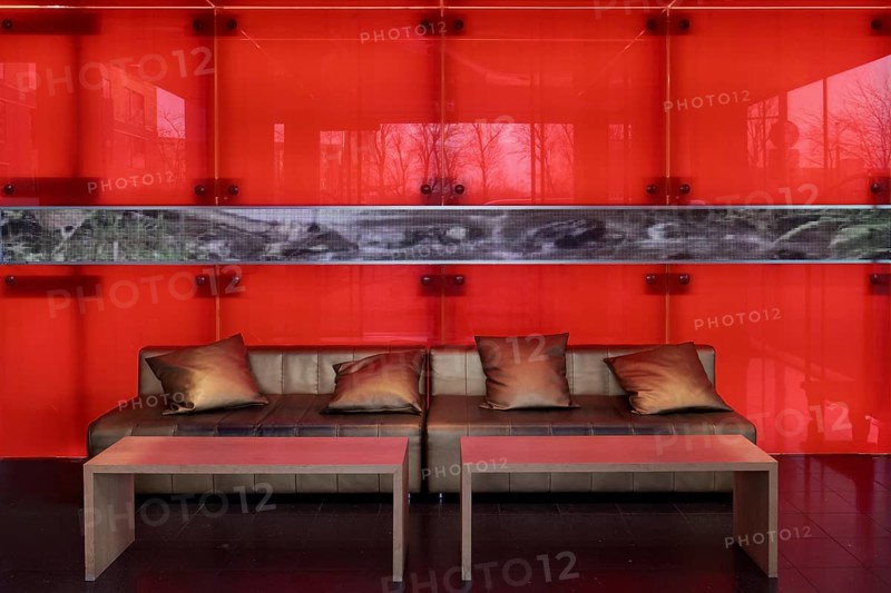 Sofa with golden cushions in front of a red-illuminated glass wall, stylish lobby of an apartment building, Düsseldorf, North Rhine-Westphalia, Germany