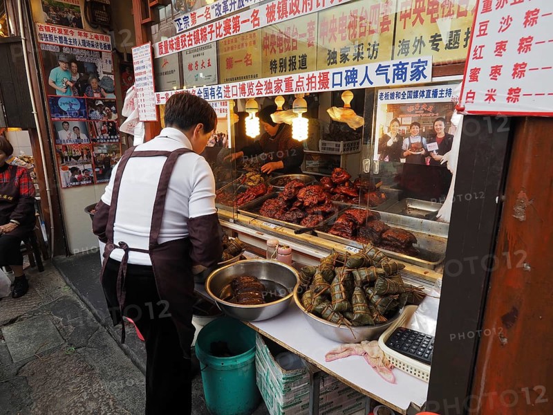 A saleswoman stands at a busy market stall with a variety of exotic foods, Zhujiajiao Ancient Town, Shanghai, China