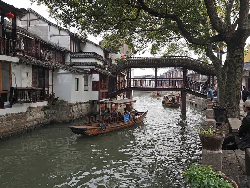 Traditional bridge over a canal with boats flanked by old houses and trees, Zhujiajiao Ancient Town, Shanghai, China