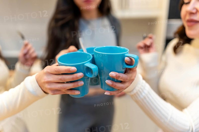 Close up of friends clinking bright blue mugs together in a warm kitchen, celebrating friendship and good vibes during a cheerful morning coffee moment