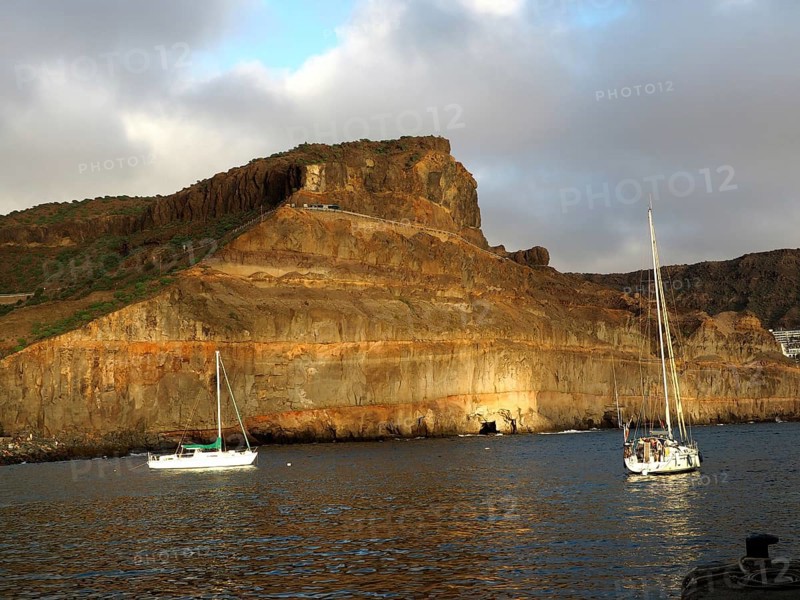Rocks on calm sea with boats and golden evening sun, Puerto de Mogan, Gran Canaria, Canary Islands, Canary Islands, Spain