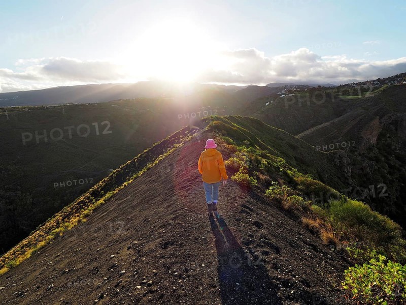 Female hiker walks along a sunlit hill with extensive shadows, Caldera de Bandama volcanic crater, Gran Canaria, Canary Islands, Spain
