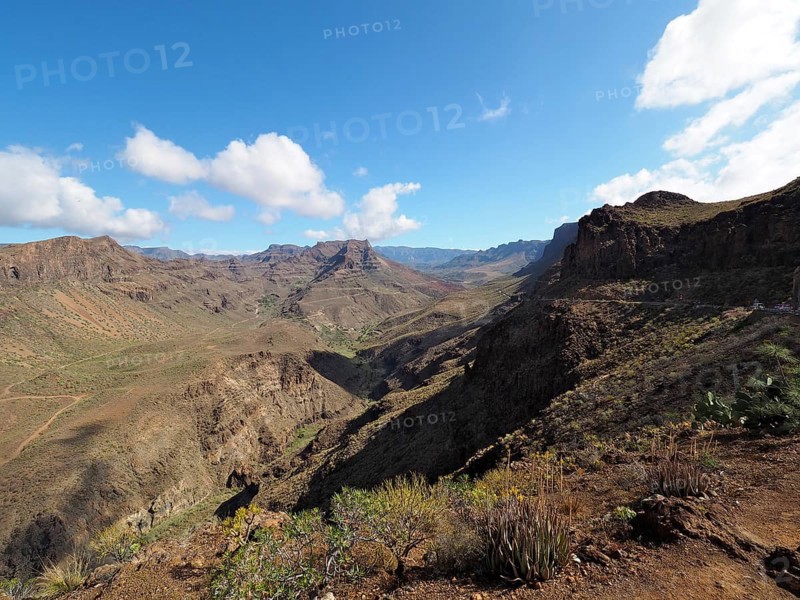 Arid mountain landscape with rocks and wide valley under a blue sky with clouds, Barranco de Fataga, Gran Canaria, Canary Islands, Spain