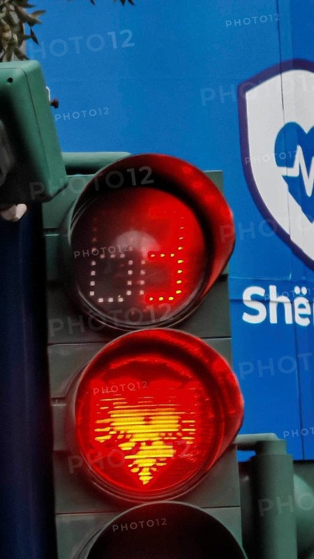 Traffic light shows red light with Tiran flag eagle against blue background in an urban environment, Tirana, Albania