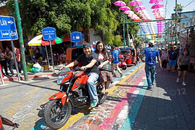Mayans wearing traditional and modern clothes on a motorcycle in an alley in San Juan la Laguna, Atitlán, Sololá Department, Guatemala