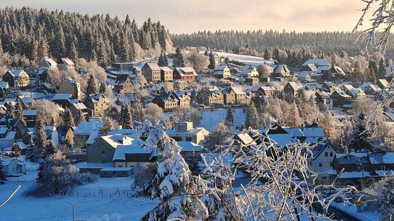 Snowy village in front of wooded hills under blue skies, Rennsteig, Thuringian Forest nature park Park