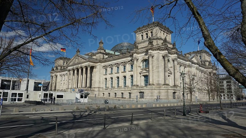 Side view of the Reichstag with flags under a blue sky, deserted during Corona, Berlin