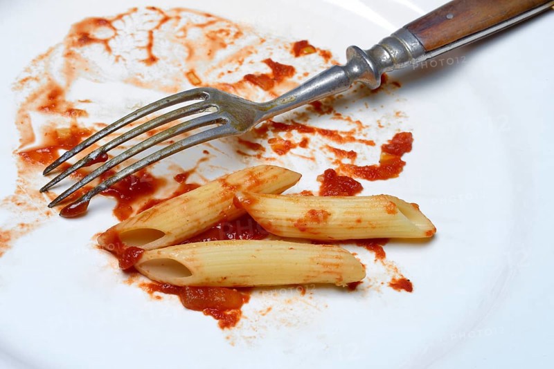Plate with fork and leftover pasta, penne and tomato sauce, food waste