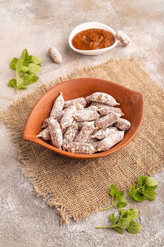 Small smoked Chicken sausages in clay bowl on brown concrete background and linen textile. side view, close up