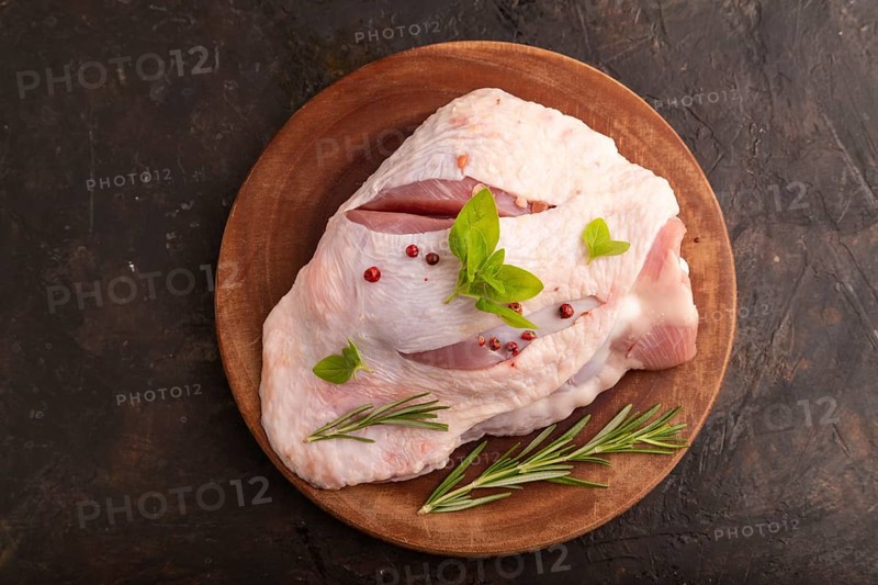 Raw Turkey Thigh with spices and rosemary on cutting board on black concrete background. top view, flat lay, close up