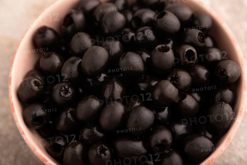 Fresh black olives in ceramic bowl on brown concrete background. side view, close up, selective focus