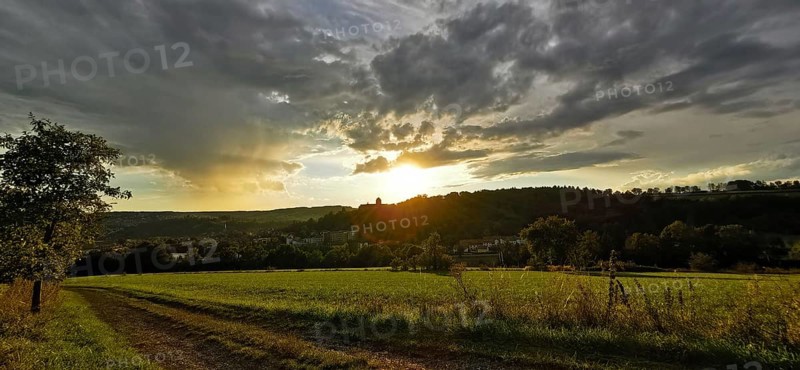 A rural scene with meadows and dirt roads at sunset, dramatic cloud formations, Franconian Forest nature park Park