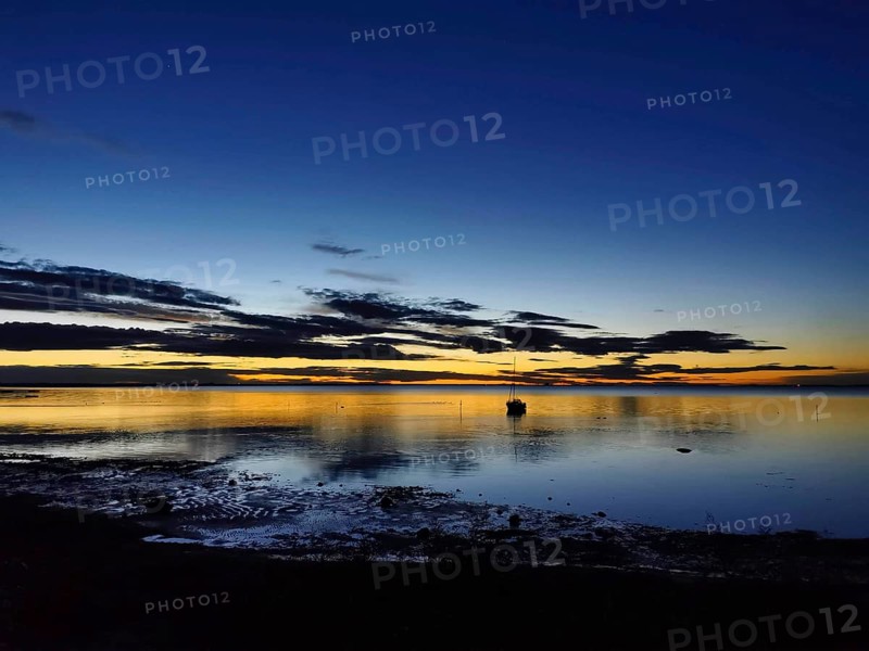 A boat on a calm lake at dusk with dramatic clouds and warm colors, Baltic Sea, Germany