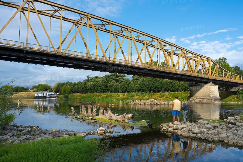 Yellow metal bridge across river with two anglers on the shore and blue sky, bridge over Morava river, Cuprija, Cuprija, Pomoravlje district, Serbia Europe