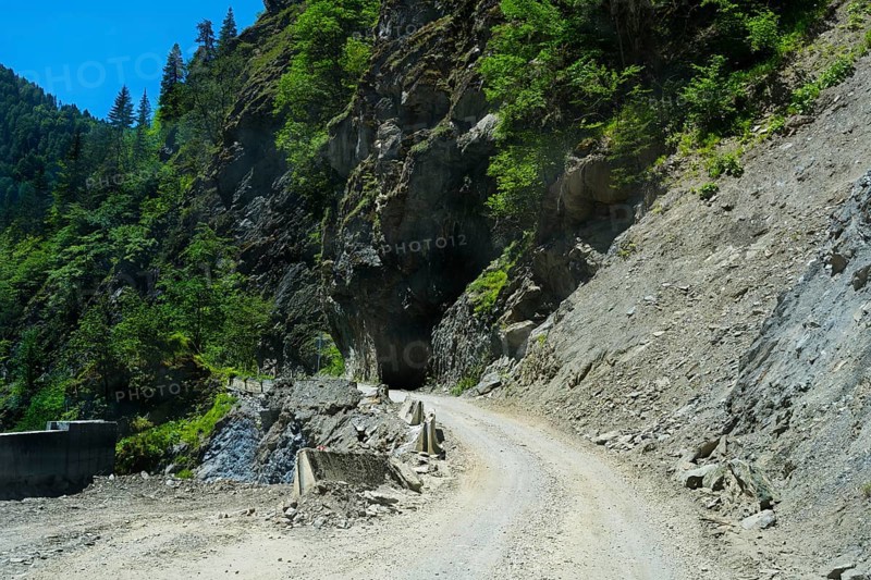 Gravel road winds around rocky mountain walls near a tunnel, road 7 partly slipped down, west of Mestia, Mingrelia region and Upper Svaneti, High Caucasus, Georgia