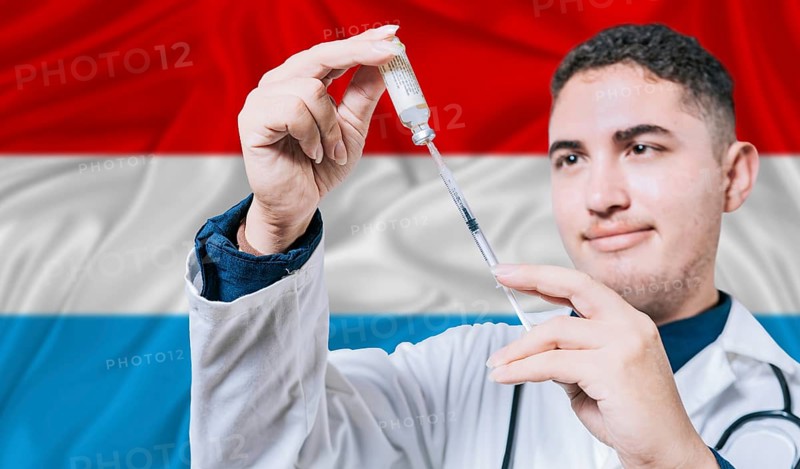 Doctor holding syringe on Luxembourg flag background. Medical professional holding syringe with Luxembourgish flag in the background