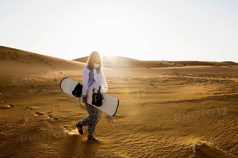 Young woman with snowboard in the sand dunes, near Merzouga, Meknès-Tafilalet region, Erg Chebbi, northern Sahara, Morocco