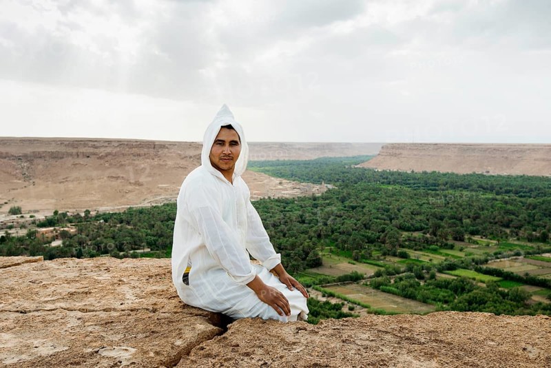 Young man and oasis in the background, near Merzouga, Meknès-Tafilalet region, Erg Chebbi, northern Sahara, Morocco