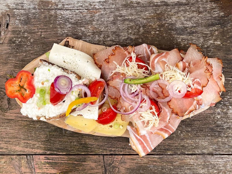 Typical snack on the alpine pasture, bacon bread and cheese bread on wooden plate on wooden table, Bavaria, Germany