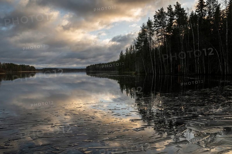 Pieces of ice and clouds reflecting on the water surface, lake in a forest, winter, Finland