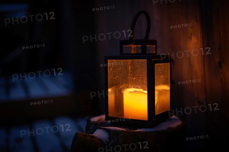 Lantern with burning candle stands on a snowy log and gives off warm light, winter, Finland