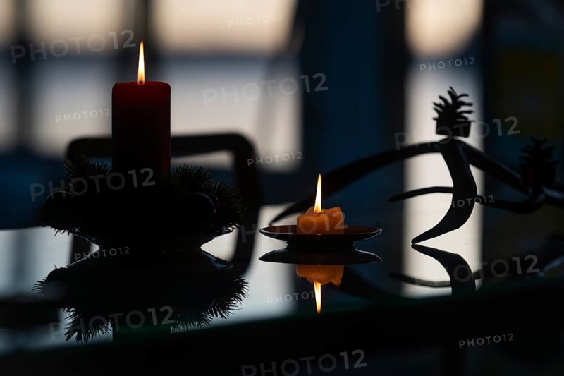 Two candles stand on a table in front of a window at dusk and create a Christmas atmosphere, plus pine branches and pine cones, Finland