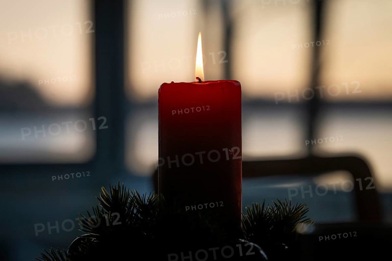 A single red candle in an advent wreath burns in front of a window at dusk and creates a cozy atmosphere, Finland